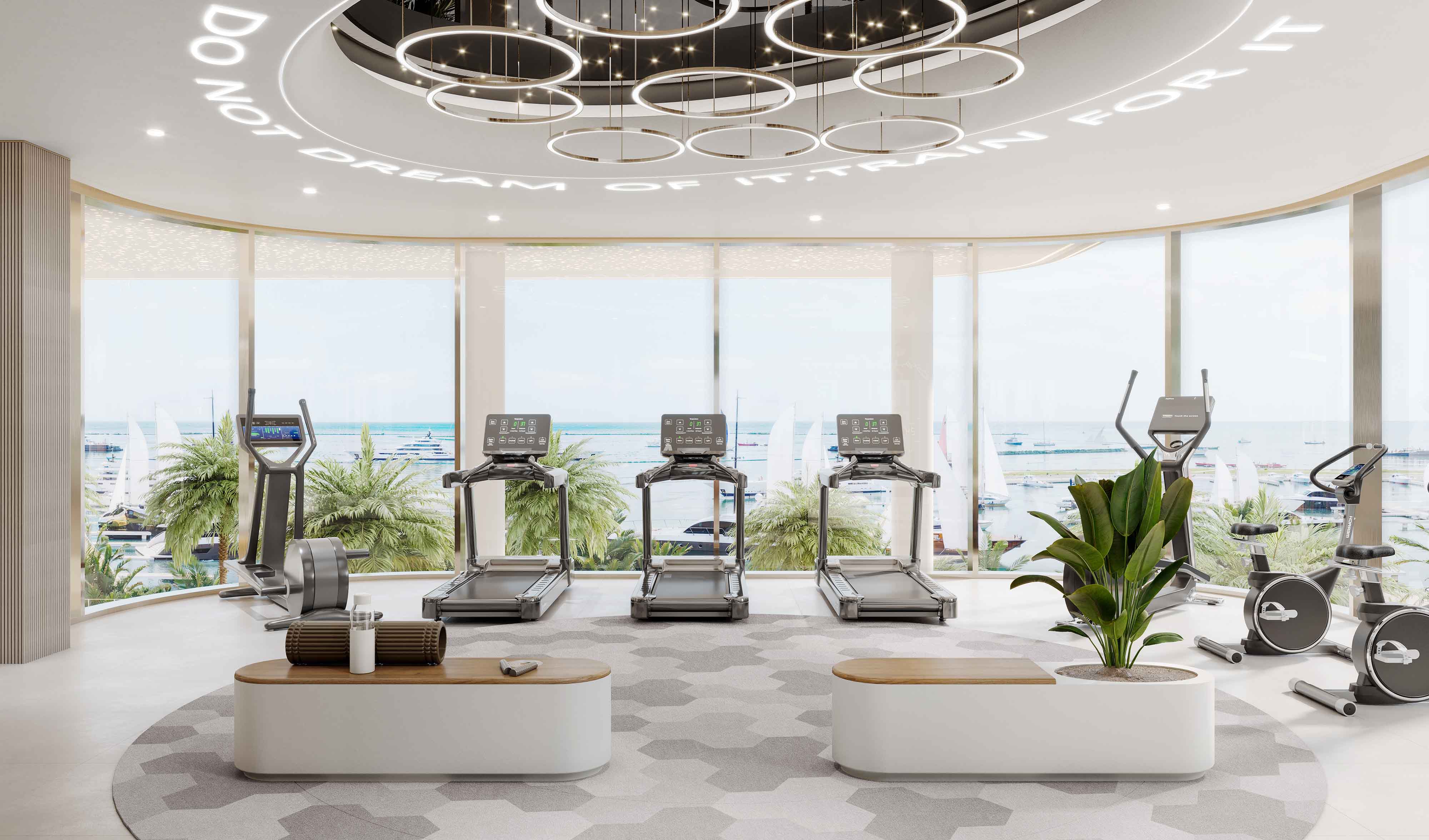 Cotier House 2 By Imtiaz A bright gym with treadmills, ellipticals, and plants, featuring large windows and a view of the sea.
